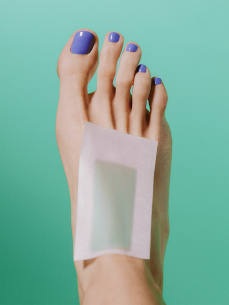 Foot with blue nail polish against a teal background with wax strip on top of foot