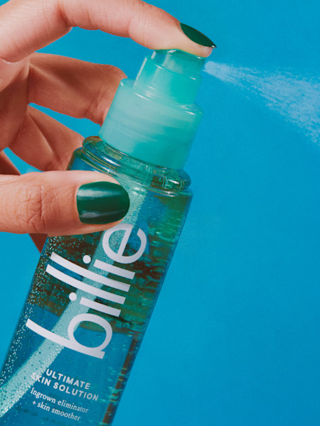 model hand with green nail polish spraying the teal ultimate skin solution spray bottle