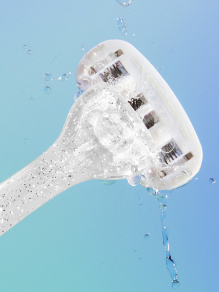 Clear plastic razor with water droplets against light blue background, showing the head with multiple blades.