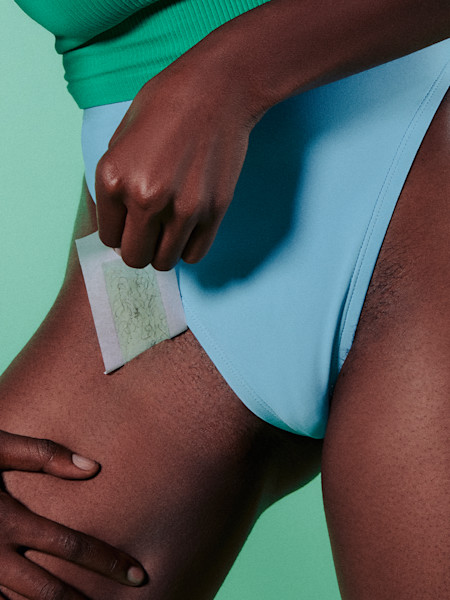 model wearing blue underwear against teal background using bikini wax strip on their bikini line