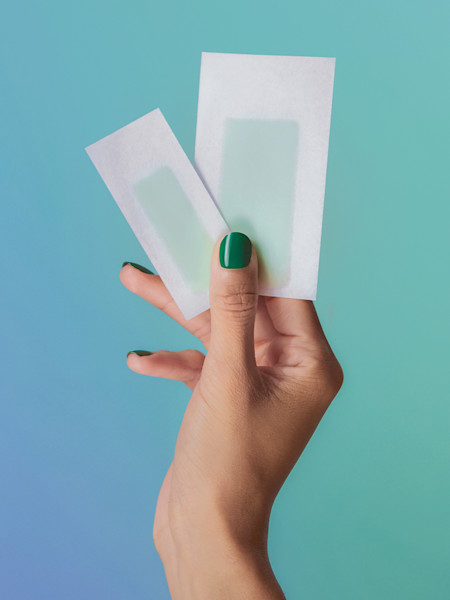 model holding a face & bikini wax strip up again a blue and green background