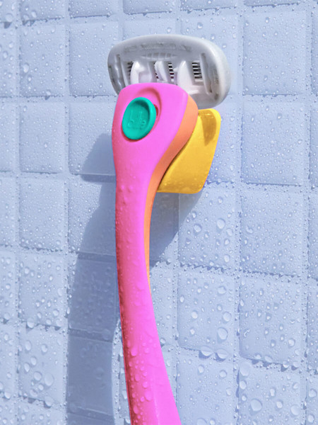 Pink and teal razor hanging on a yellow magnetic holder on a white shower tile