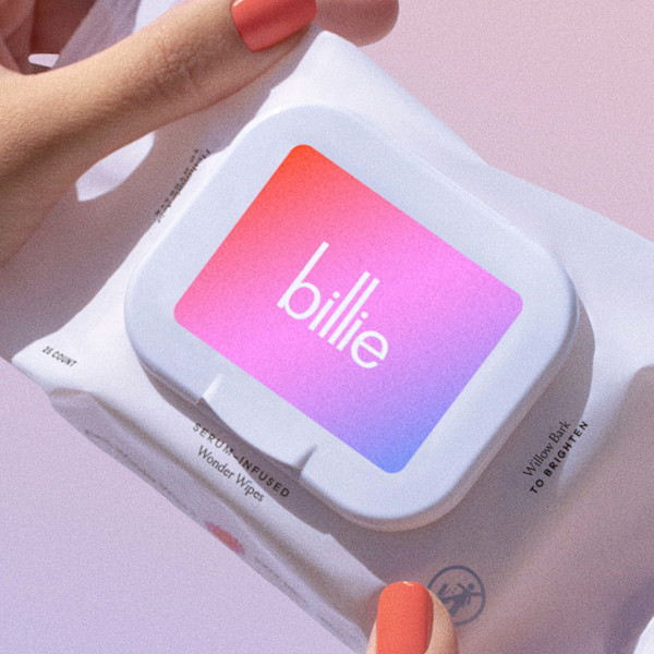 Hand with coral nails holding Billie serum-infused Wonder Wipes package with pink-to-purple gradient logo.