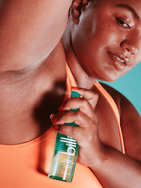 Model wearing an orange sports bra using teal ultimate skin solution spray on their underarm