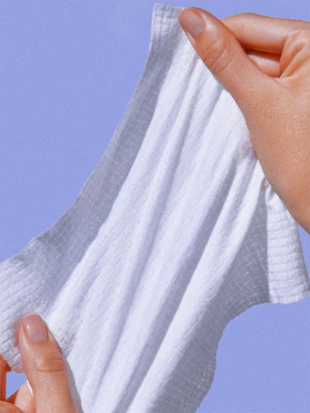 Hands holding a white textured cloth or washcloth against a light blue background.