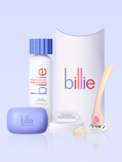Billie shaving products including purple body buffer soap, whipped shave cream bottle, razor, and packaging on light blue background.