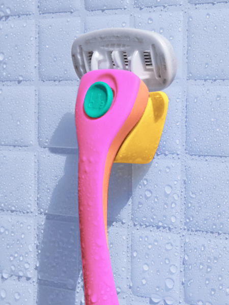 pink, orange, and teal razor on the yellow magnetic holder on a white shower tile