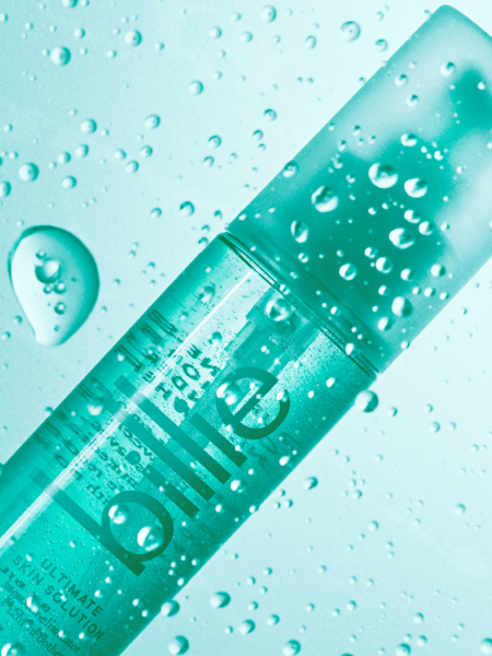 Teal ultimate skin solution spray bottle against a teal background with water drops