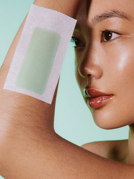 Woman holding side of arm up against a teal background with a wax strip placed on arm